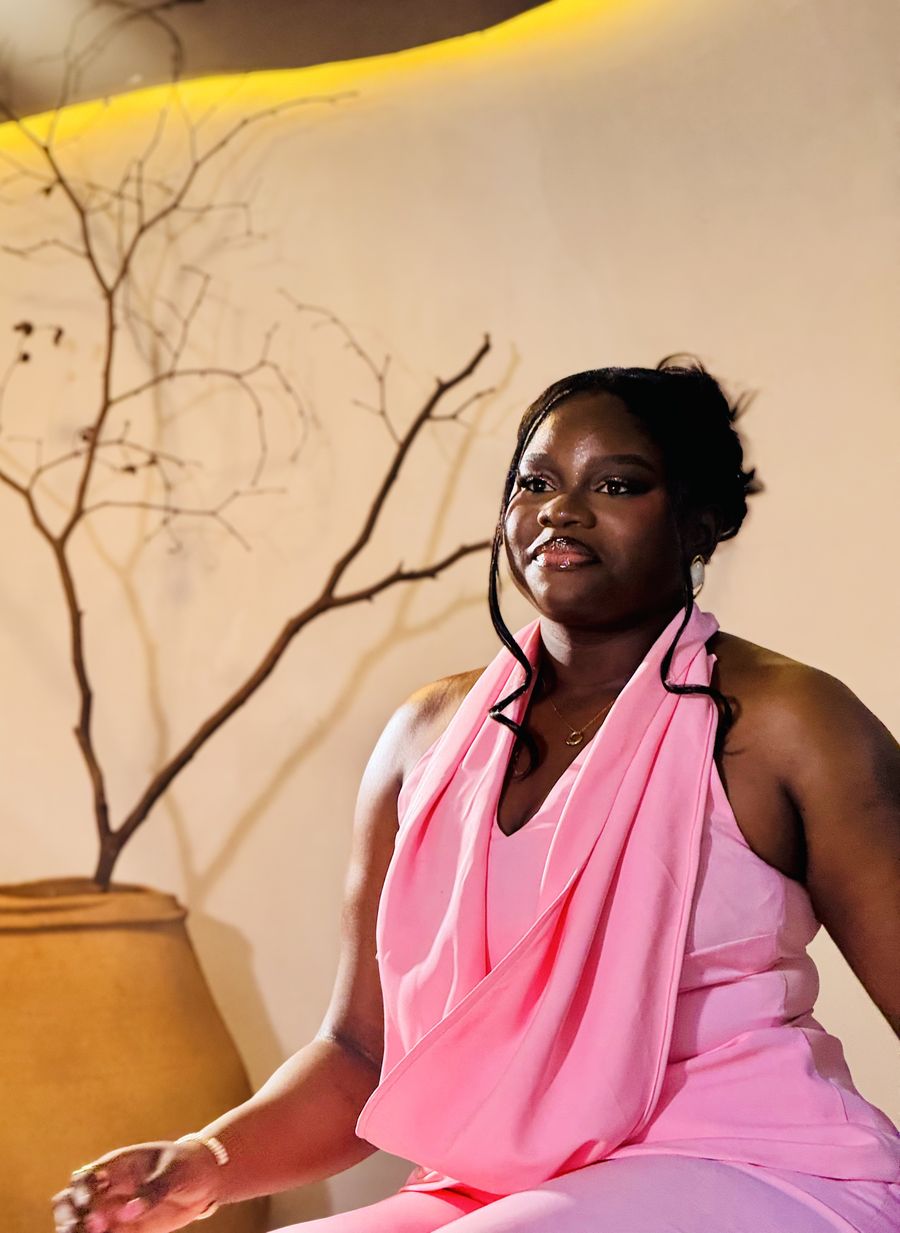 Adeoti Osifeso, founder of Shaping Influence Africa, seated in a warm room beside a vase of bare branches